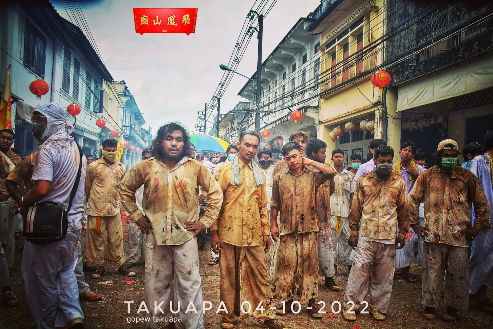 คณะหามเกี้ยวในชุดที่เปรอะจากการแห่ ยืนถ่ายภาพหมู่กลางถนนเมืองเก่าที่ประดับโคมแดง